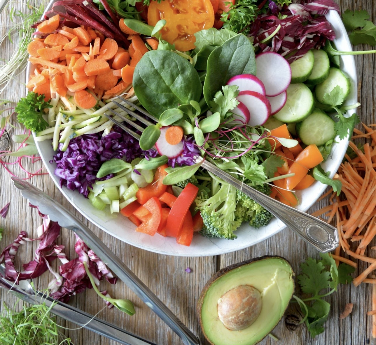 色とりどりの生野菜を盛り付けたサラダボウル。にんじん、きゅうり、ラディッシュ、紫キャベツ、ブロッコリー、ベビーリーフなどが円形に並び、横にカットしたアボカドが添えられている食卓風景