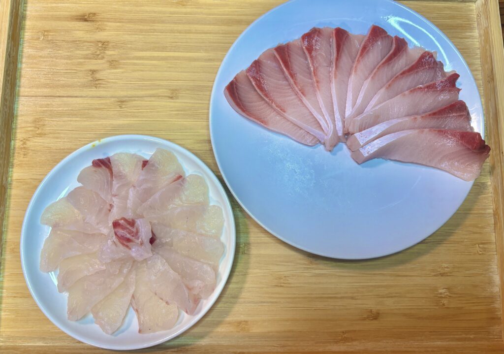木のまな板の上に置かれた白身魚のお刺身。大皿には厚めに切った切り身、小皿には薄造りが美しく並んでいる
