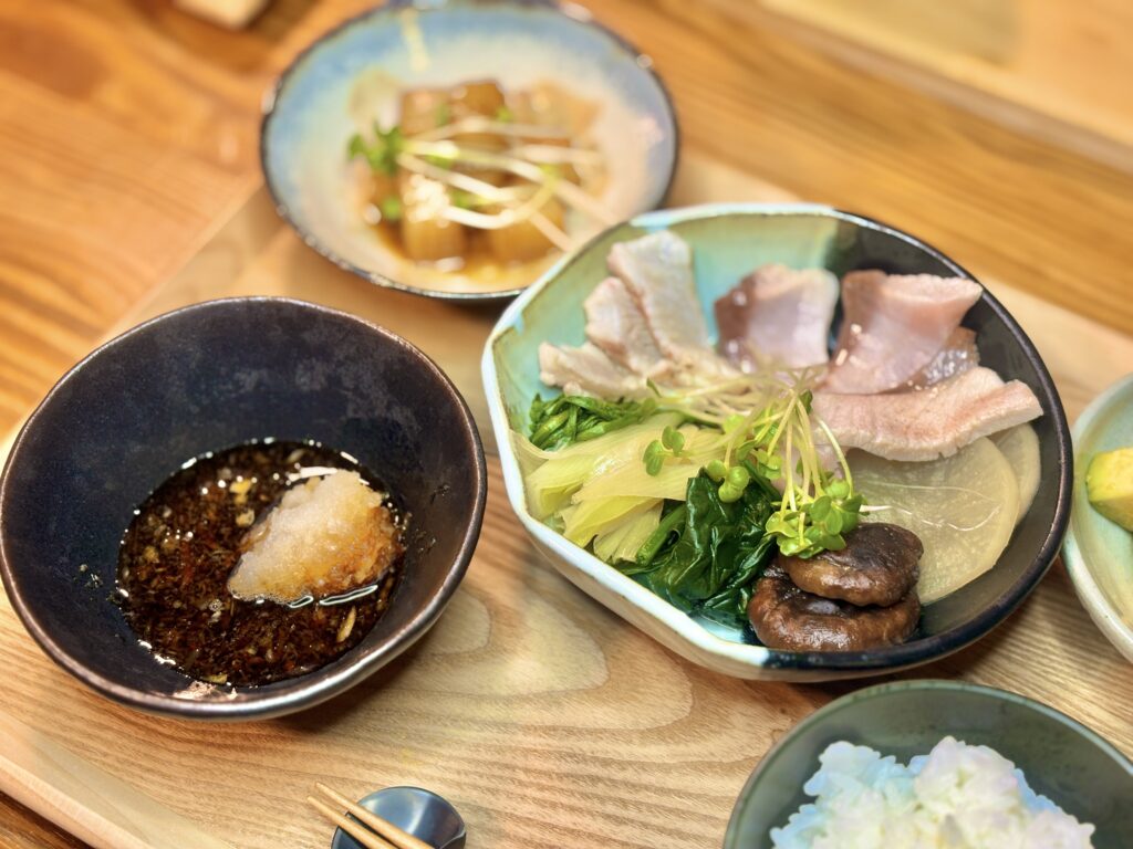 木のトレーに並んだ和定食。白身魚の湯引き、青菜ときのこ、大根の煮物、ごはん、小鉢がそろった家庭料理