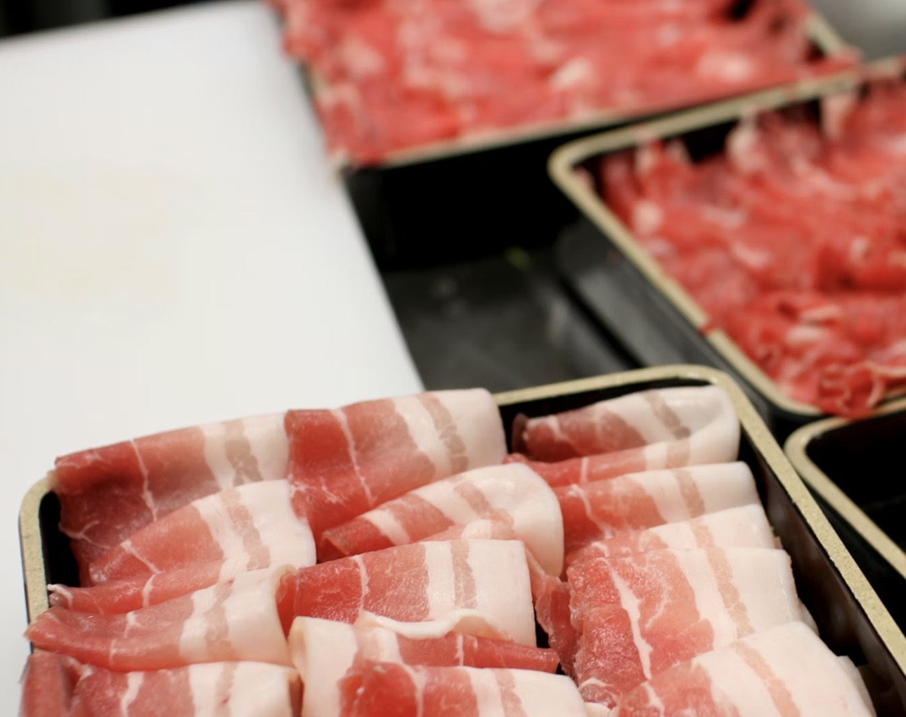 黒いトレーにきれいに並べられた薄切りの豚バラ肉、赤身と白い脂の層がはっきり見える ② しゃぶしゃぶ用の豚バラ肉が整然と並び、上質な脂の入り方が分かる接写写真