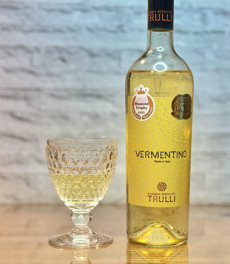 イタリア産白ワイン「ヴェルメンティーノ」と、カットグラスに注いだ淡い黄金色のワインを並べたテーブルフォト。ラベルには金色のデザインと受賞マークが見える