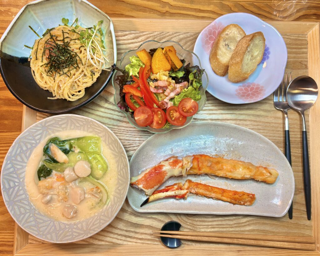 タラバガニのバターソテー、ホタテとカニと青梗菜のクリーム煮、明太パスタ、かぼちゃとパプリカのサラダ、バゲットを並べた豪華な食卓の全体写真。