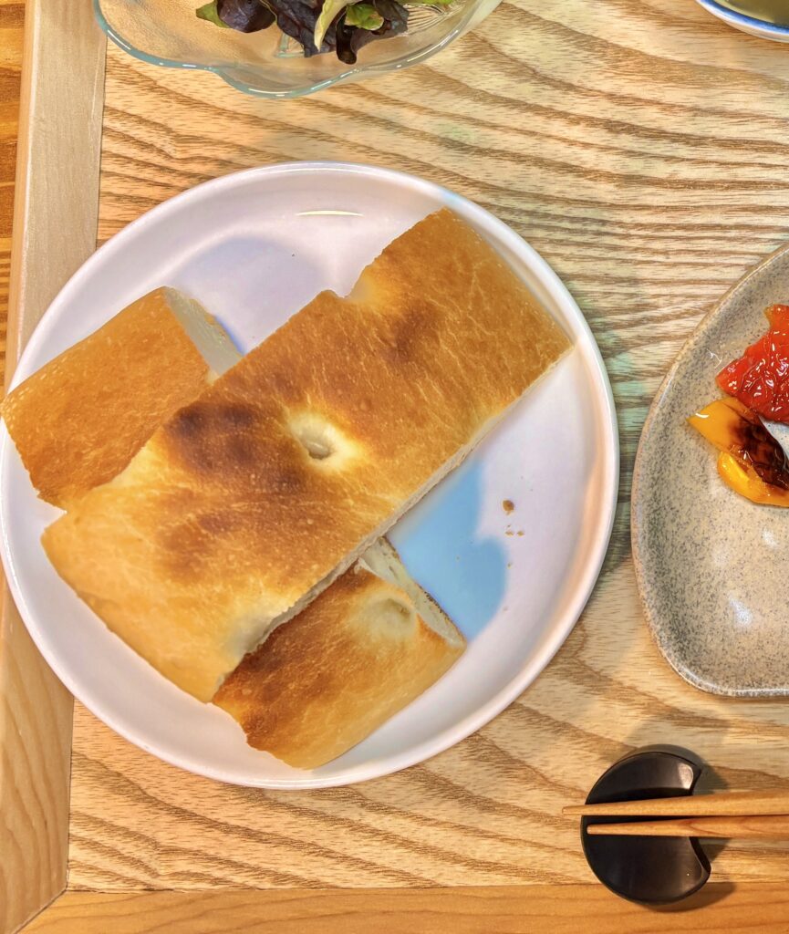 白い皿に盛り付けたフォカッチャをカットして並べた一皿。こんがり焼き色のついたパンが木製トレーの上に置かれた、おうちビストロ風ディナーの一場面。
