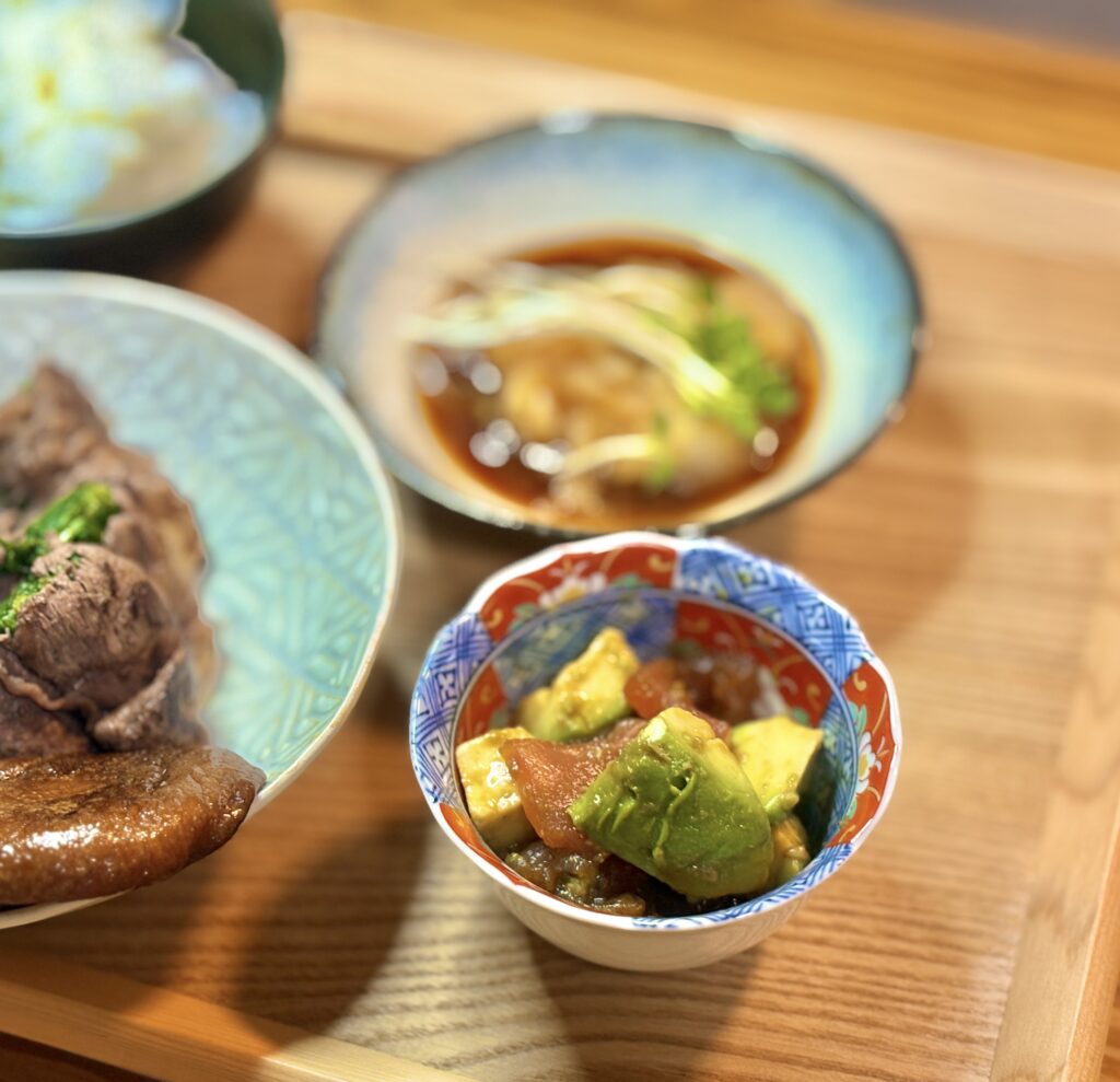 小さな和柄の器に盛り付けた、角切りのアボカドとマグロをわさび醤油で和えた副菜。アボカドの鮮やかな緑とマグロの赤身が映える、さっぱりとした和風の一品