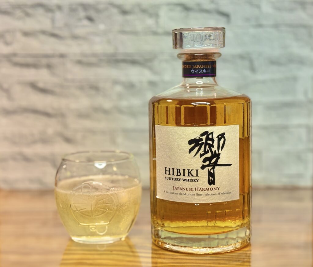 木のテーブルの上に置かれたサントリーウイスキー響 ジャパニーズハーモニーのボトルと、グラスに注いだウイスキーの写真。