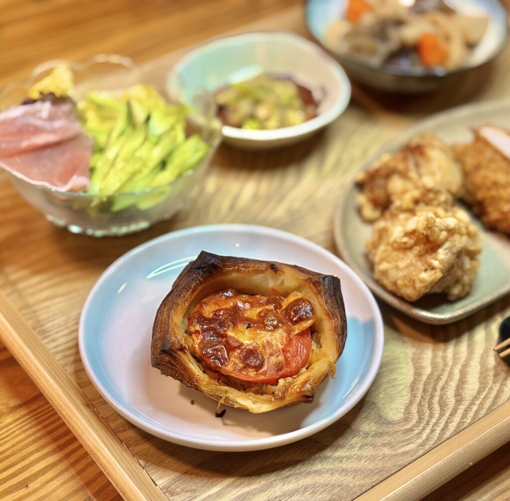 小皿に盛り付けたリョウイチヤマウチのトマトとツナのパン。焼き色のついたデニッシュ生地にトマトとツナがのり、木目のテーブルに置かれている料理写真