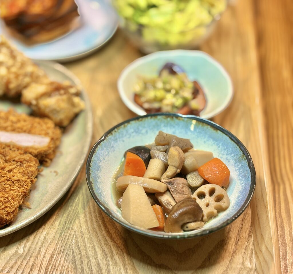 小鉢に盛り付けられた博多の郷土料理がめ煮。れんこん、にんじん、里芋、ごぼう、鶏肉、しいたけなどの具材が煮汁を含んで艶やかに見える料理写真