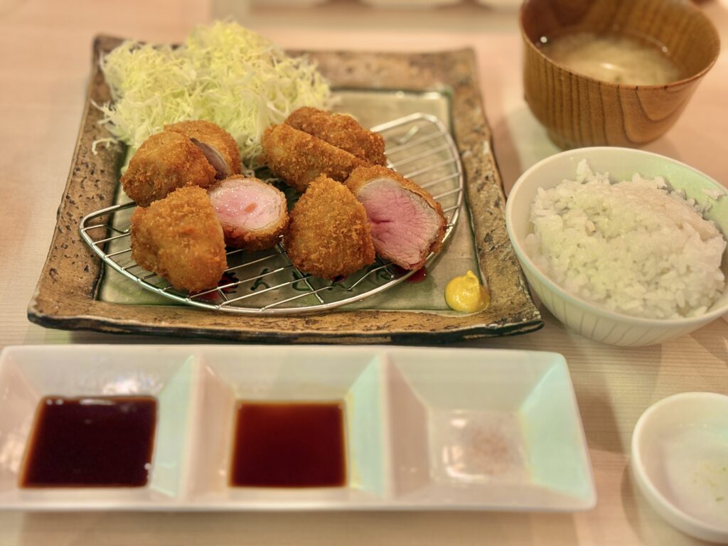 レアに揚がった一口サイズのとんかつがカットされ、ピンク色の断面が見える定食。千切りキャベツ、ご飯、味噌汁、3種の調味料が並ぶとんかつ専門店の昼食。
