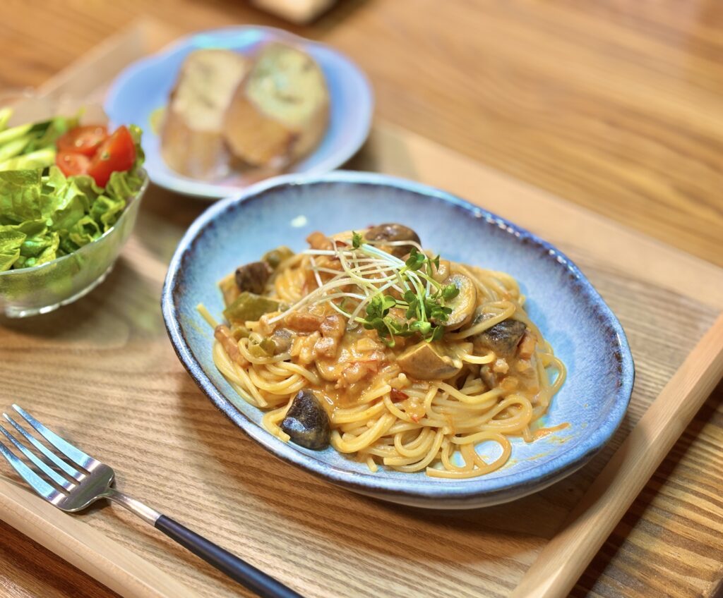 木製トレーの上に盛り付けられた椎茸とマッシュルーム、ベーコンのトマトクリームソースパスタ。青い器に盛られ、上にスプラウトがのった旦那キッチンの夜ごはん。
