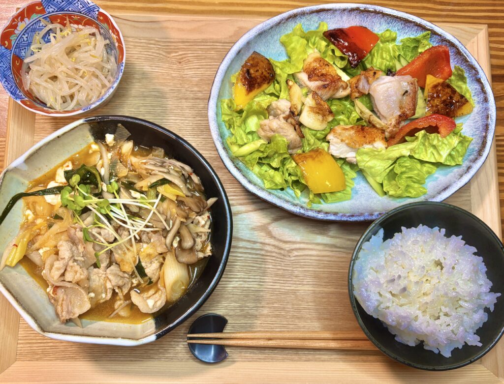 豚肉チゲ、パプリカとチキンソテーのサラダ、もやしナムル、ご飯が並んだ晩ごはんの食卓全体写真