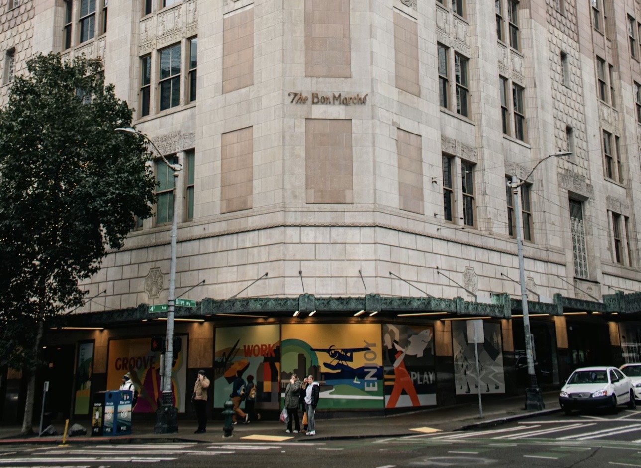 交差点の角に建つアールデコ調の石造りの建物の外観。1階部分にはカラフルなグラフィックが描かれ、歩道には数人の歩行者が立っている。