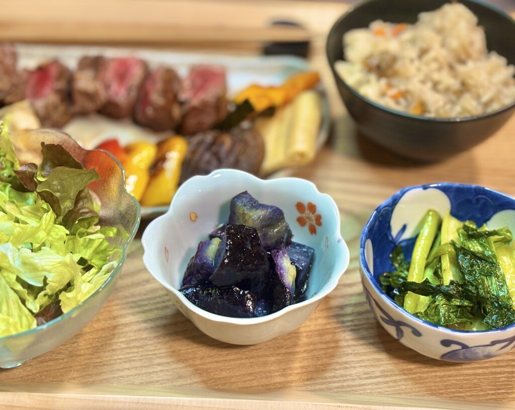 アンガス牛ステーキ献立の彩り副菜。中央は作り置きの茄子の揚げ浸し、右はシャキシャキ食感の小松菜のガーリック炒め。左にサラダも添えた、野菜たっぷりの定食スタイル。