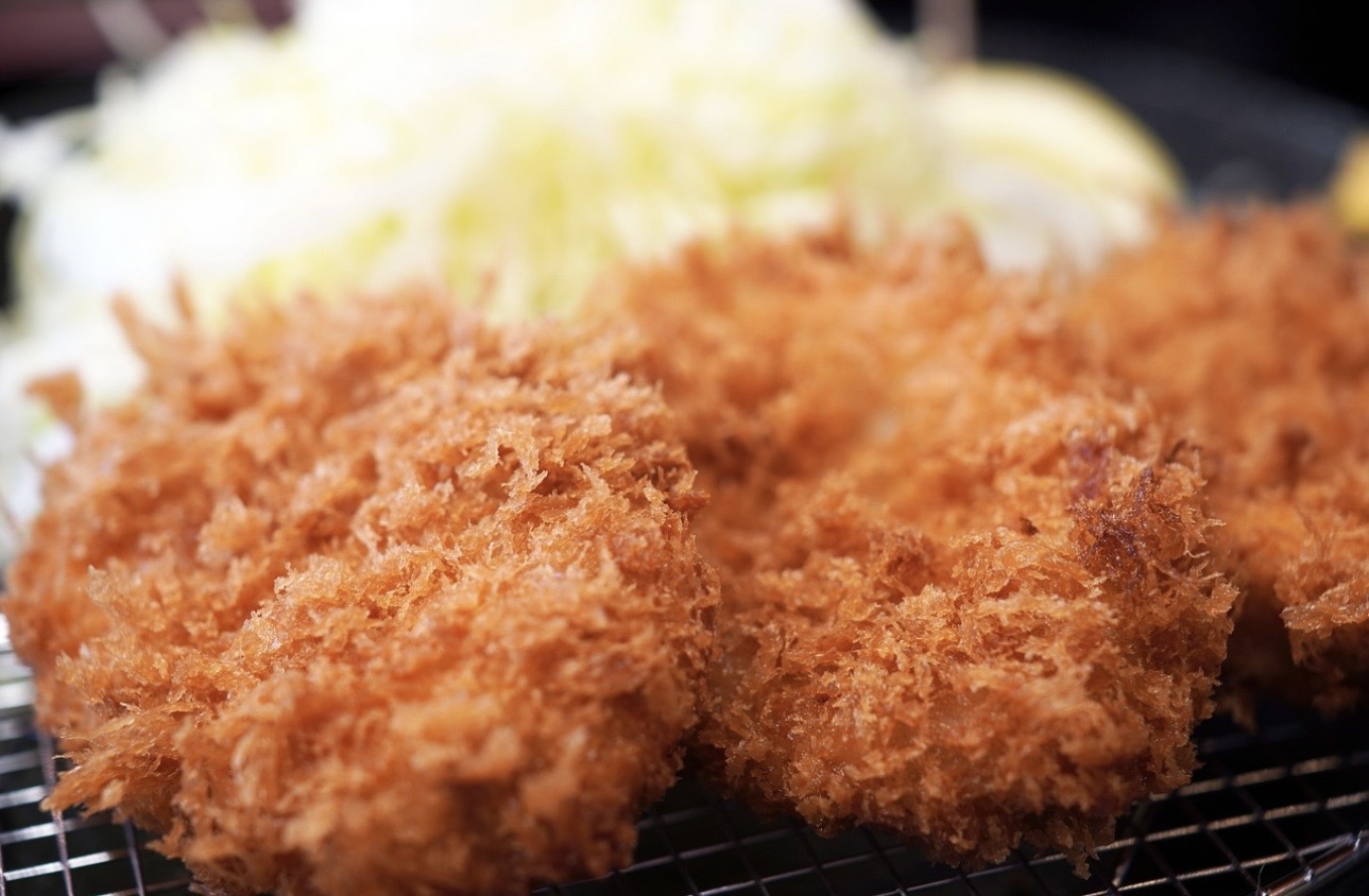 衣がサクサクに揚がったとんかつが網の上に並び、奥には刻みキャベツが添えられている料理写真