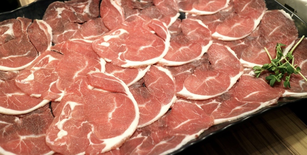 黒い器に並べられた、生のラム肉のスライス。赤身と白い脂身のコントラストが美しく、端にハーブが添えられている料理写真