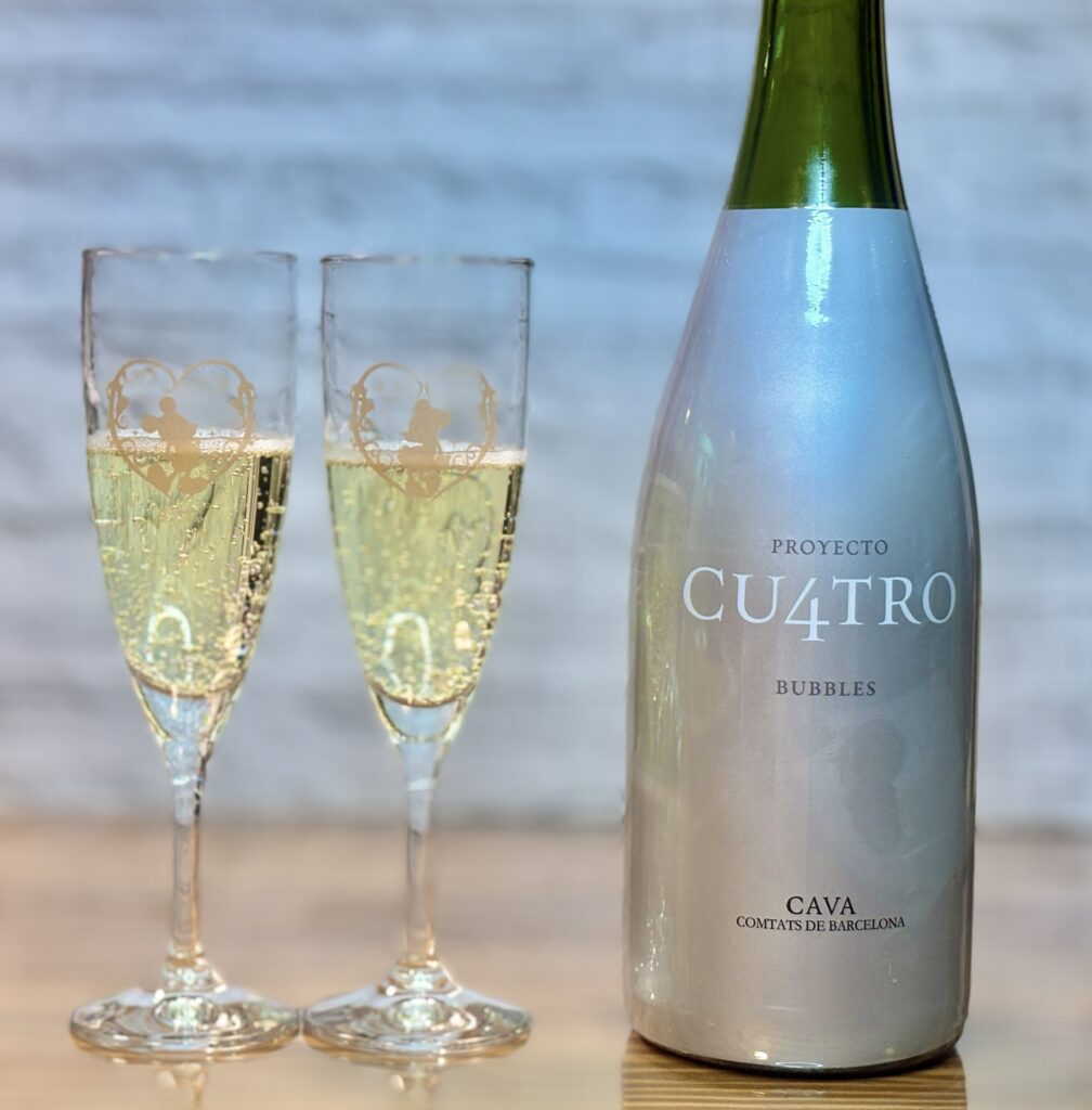 シルバーのボトル「プロジェクト・クワトロ・カヴァ」と、ミッキー&ミニーのハートが描かれたペアグラス。グラスには黄金色のスパークリングワインが注がれ、細かい泡が立ち上っている。