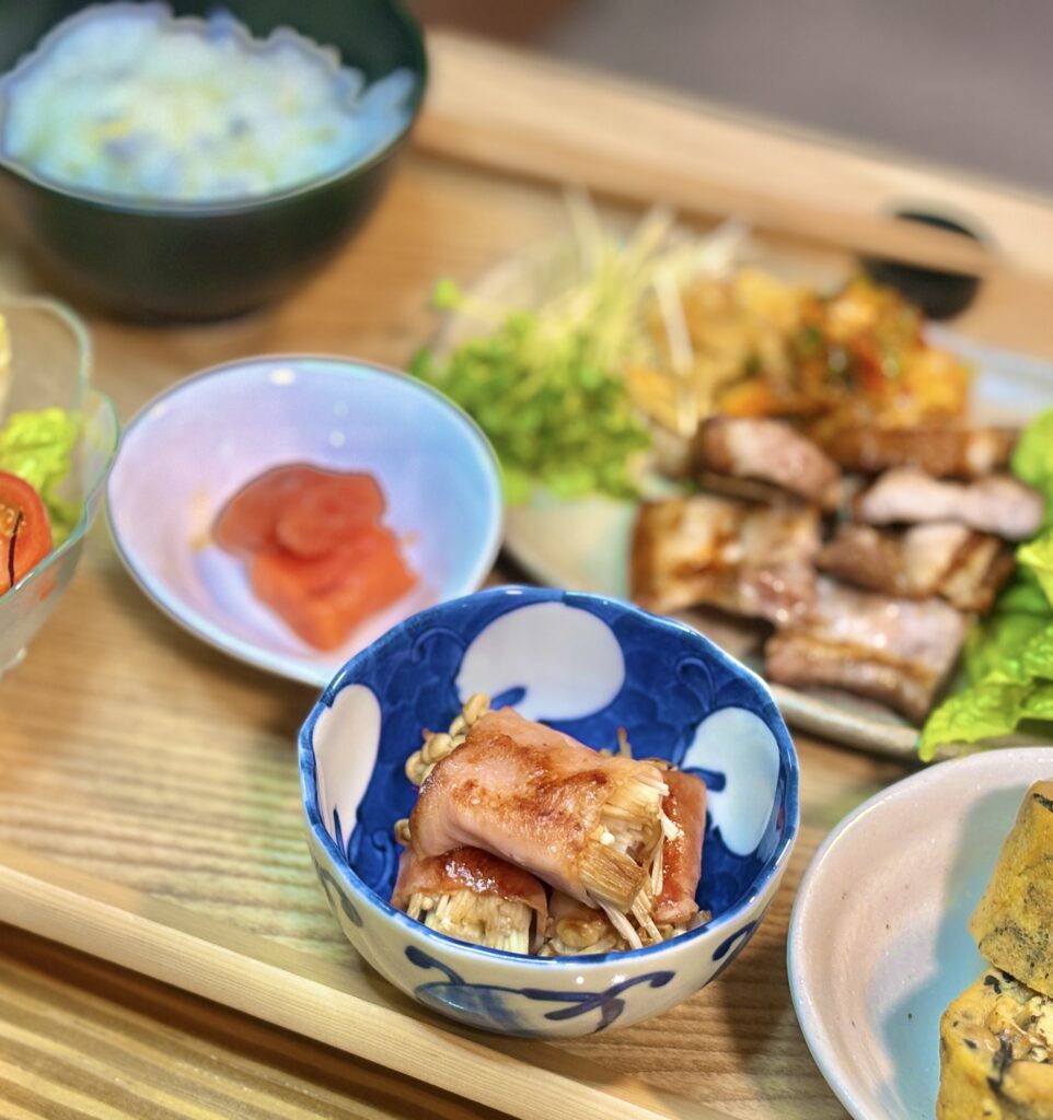 えのきをベーコンで巻いて香ばしく焼き上げた副菜が、藍色の模様が入った小鉢に盛り付けられている様子。