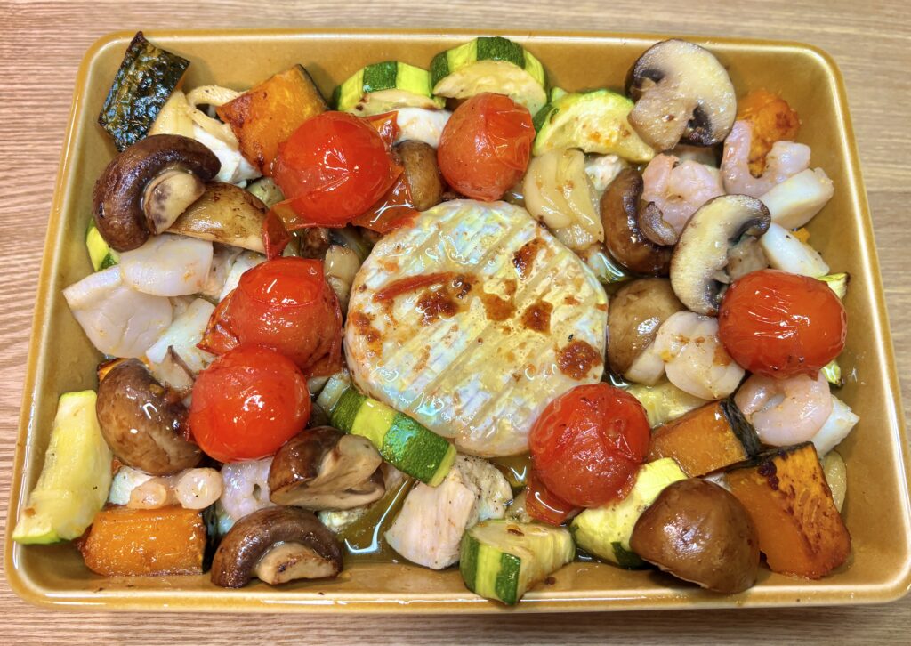 耐熱皿いっぱいの海老、マッシュルーム、ズッキーニ、かぼちゃ、トマトの中央で、こんがり焼き色のついた丸ごとカマンベールがとろける豪華なアヒージョ。