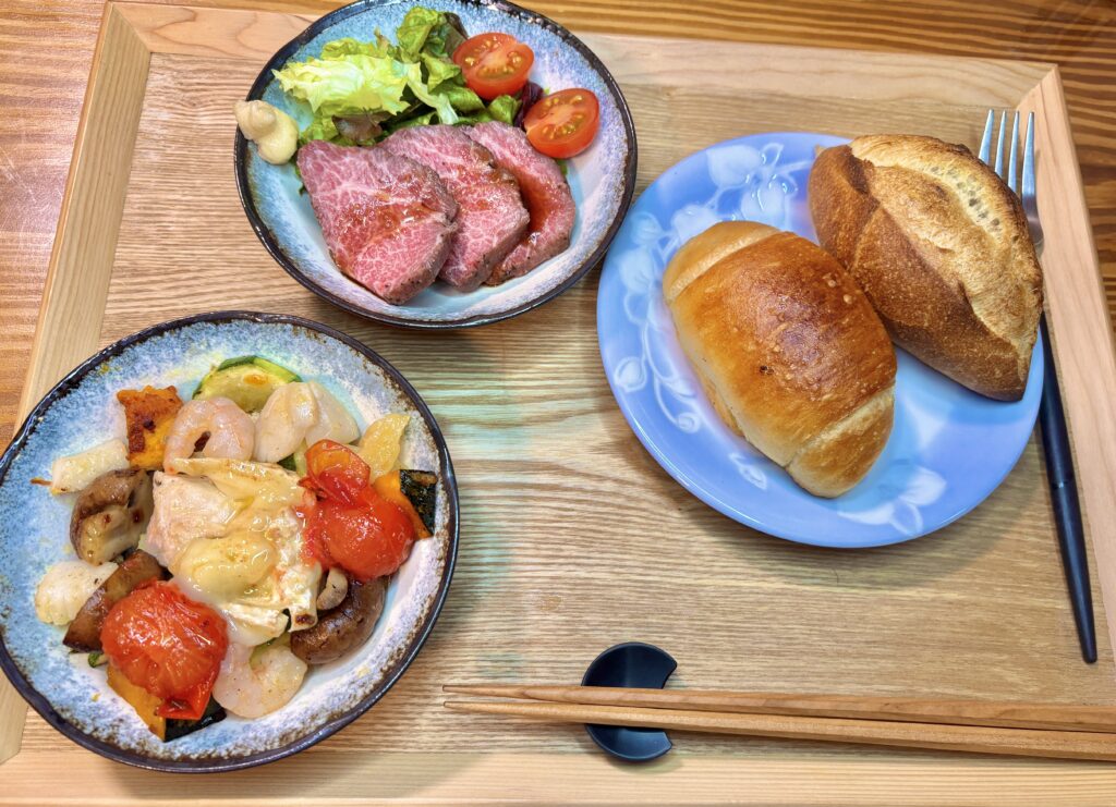 木製トレイに美しく並んだ、アヒージョ、ローストビーフサラダ、そしてダンマルシェのパン。旦那様のこだわりが詰まった、おうちで楽しむ豪華ビストロセット。