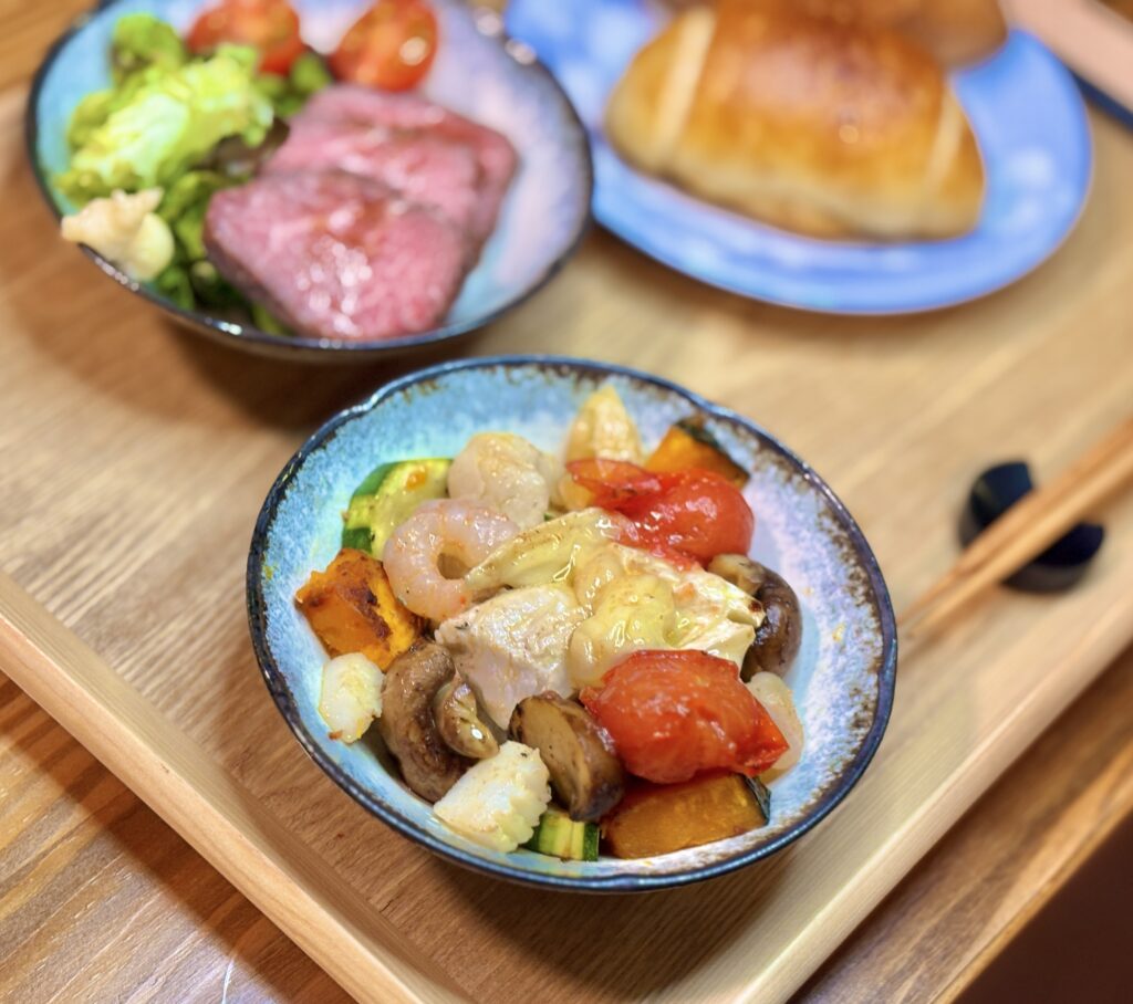 小皿に取り分けられた、カマンベールチーズと彩り豊かな夏野菜、シーフードのアヒージョ。オリーブオイルに具材の旨味が溶け出した、食欲をそそる一枚。