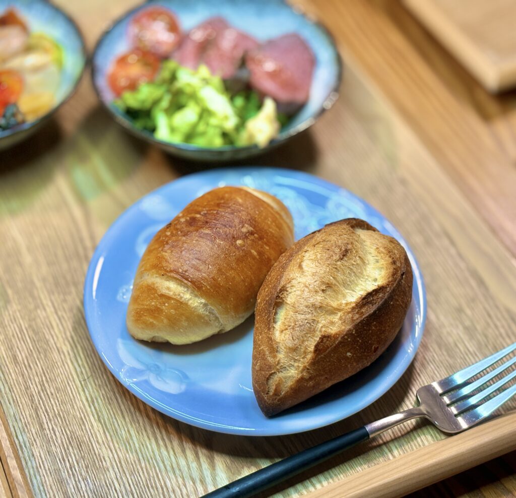 「ダンマルシェ」で購入した、アヒージョのオイルにぴったりの香ばしいバゲットと、外はカリッと中はもっちりした塩パンが乗った、爽やかな青い皿。