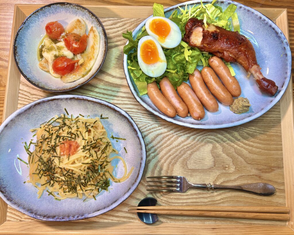 青い器に盛り付けられたローストチキンとシャウエッセン、半熟卵のサラダ。レタスの上に骨付きチキンとソーセージ5本が乗った、ボリューム満点の旦那ごはん