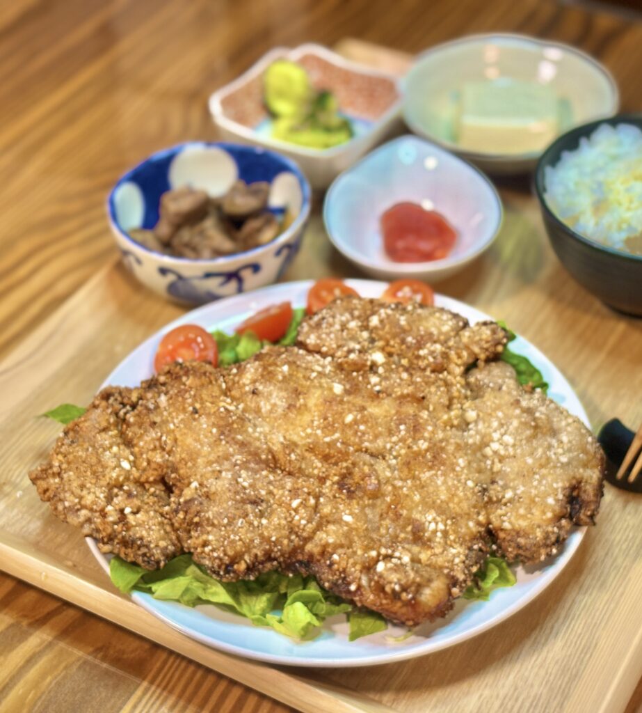 網の上に乗った、揚げたてで衣がサクサクとした巨大な台湾唐揚げダージーパイと、横に添えられた白ごはんのアップ
