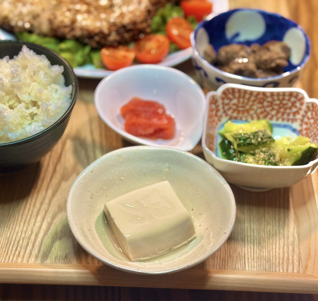 左手前のベージュの小鉢に入った冷奴、中央の白いしずく型の器の明太子、右側の赤い柄の四角い小鉢に入った叩ききゅうりの副菜3種が並ぶ様子
