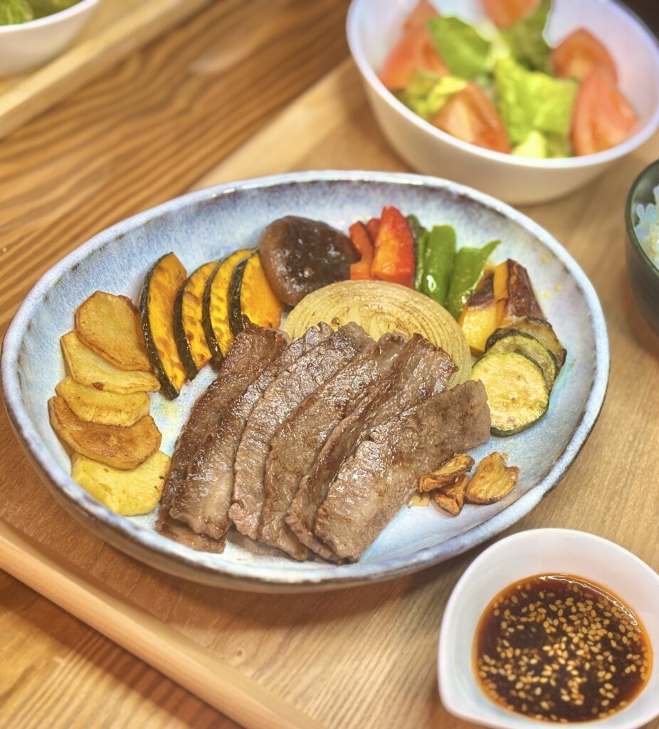 青い皿に盛り付けられた、こんがりと焼けたジューシーな牛肉の焼肉と、カボチャ、玉ねぎ、しいたけ、ピーマンなどの焼き野菜のクローズアップ
