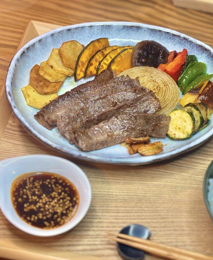 青い皿に盛り付けられた、こんがりと焼けたジューシーな牛肉の焼肉と、カボチャ、玉ねぎ、しいたけ、ピーマンなどの焼き野菜のクローズアップ
