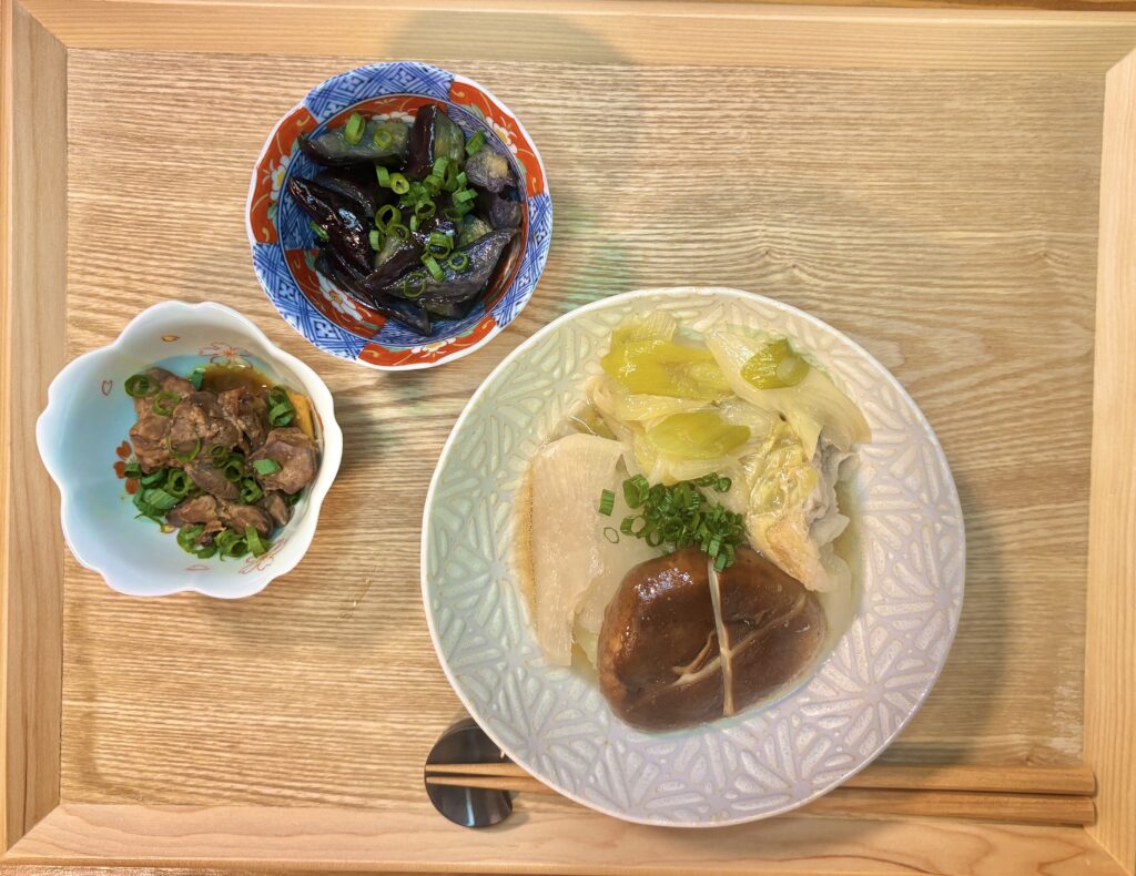 木製のお盆の上に、取り分けたミルフィーユ鍋の器、揚げ出し茄子、鳥レバーの甘露煮がバランスよく並んでいる。箸置きと箸も添えられ、一人分の食卓として整えられている。