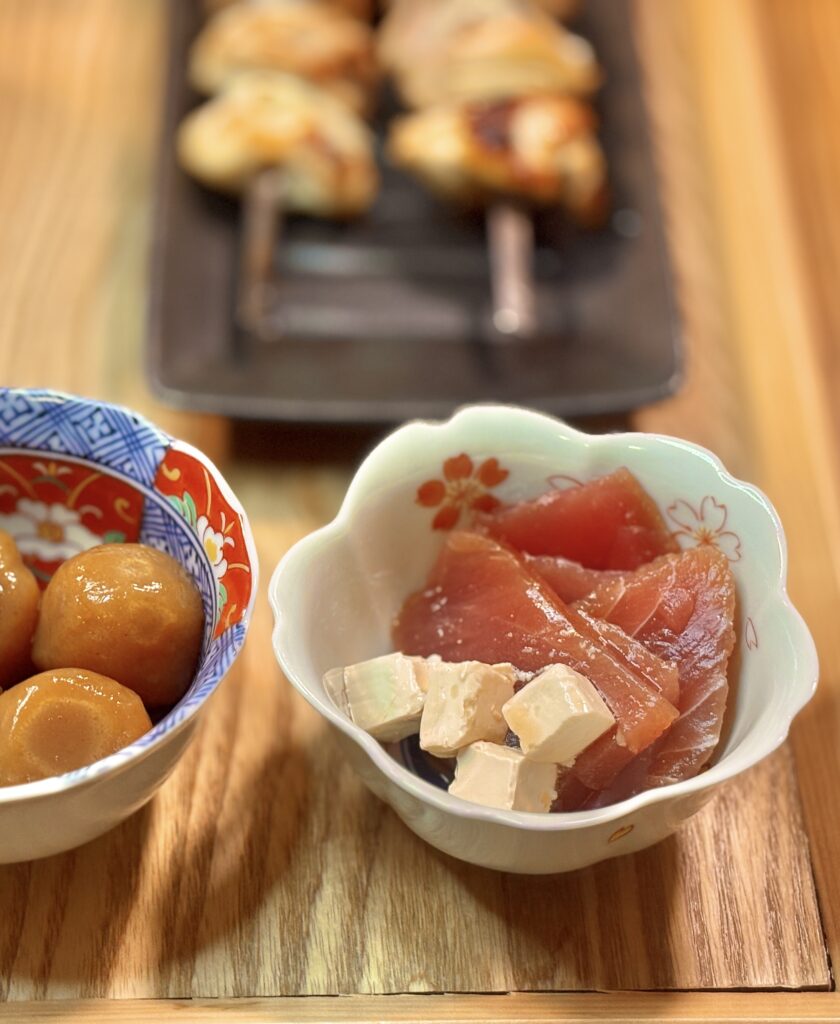 白い小鉢に、出汁醤油に漬けたキハダマグロと角切りのクリームチーズを盛り付けた写真。マグロの赤身とチーズの白のコントラストが印象的。
