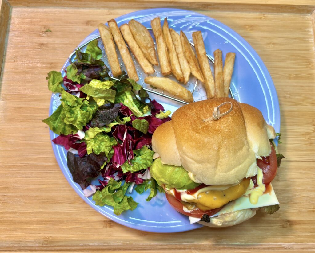 水色の皿に、手作りハンバーガーとミックスリーフのサラダ、フライドポテトがバランスよく盛り付けられている。
ハンバーガーのバンズの上にはピックが刺さり、具材のボリューム感が伝わる構図。