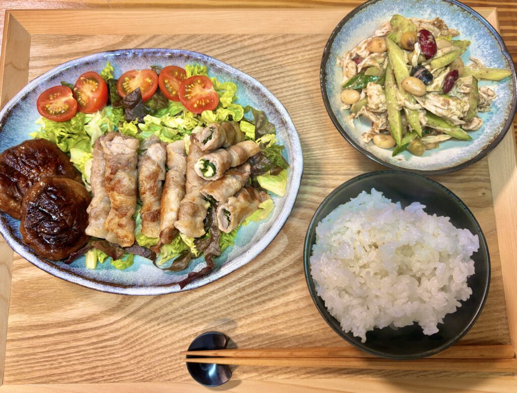 木製トレイの上に、豚ロースの紫蘇チーズ巻きと焼き椎茸を盛り付けたワンプレート、アボカド入りバンバンジー、ご飯を並べた家飲み晩ごはんの全体写真
