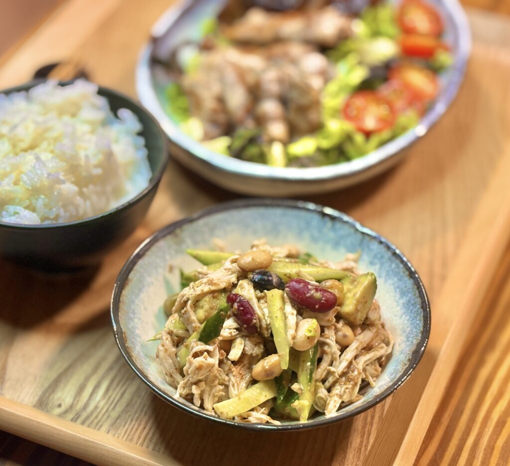 アボカドとミックスビーンズを合わせたバンバンジーを器に盛り付けた副菜のアップ、奥にぼんやり見えるメインプレートとご飯
