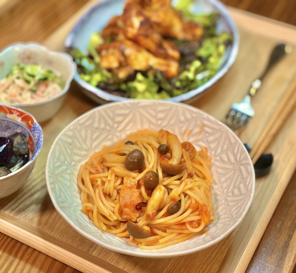 しめじとベーコン入りのガーリックトマトパスタのアップ。トマトソースが絡んだパスタにきのことベーコンがバランスよく混ざっている。