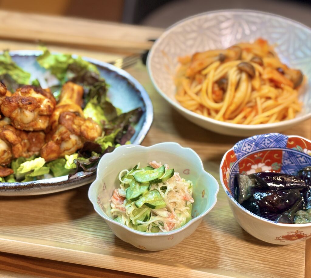 小鉢料理を中心に写した写真。手前にカニカマときゅうりのさっぱり和え物、奥にタンドリーチキンとパスタがぼんやり見える構図。