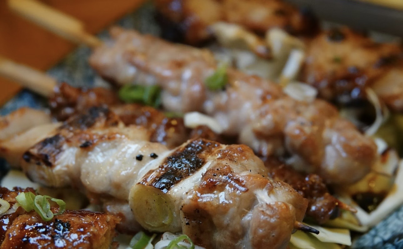 香ばしく焼き上げた鶏肉と玉ねぎの焼き鳥を間近で写したクローズアップ写真。照りのある焼き目と肉汁が伝わり、刻みねぎが散らされていて、手作りならではの臨場感が感じられる。