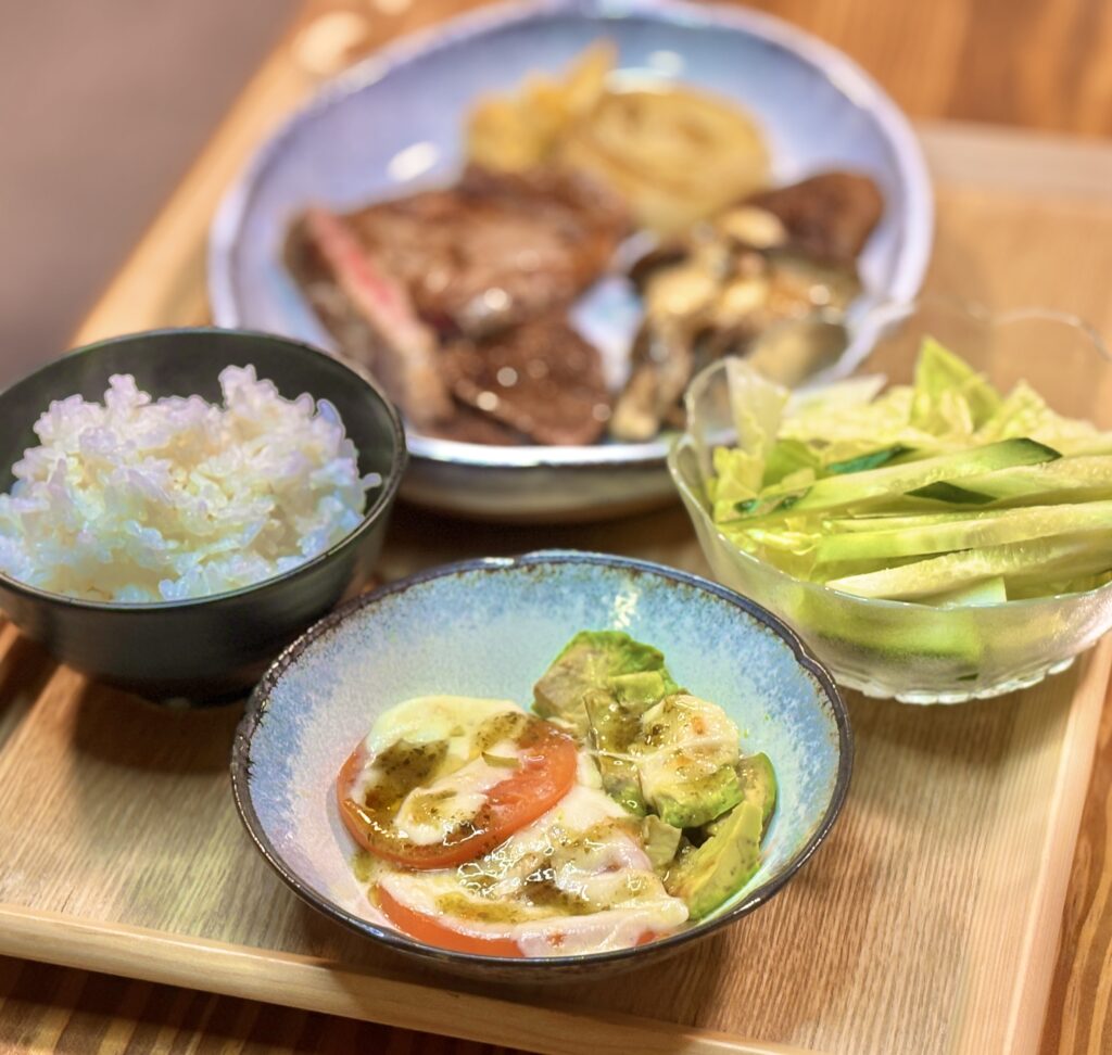 トマトとアボカドのモッツァレラチーズ焼きにバジルソースをかけた小鉢と、奥にステーキ定食