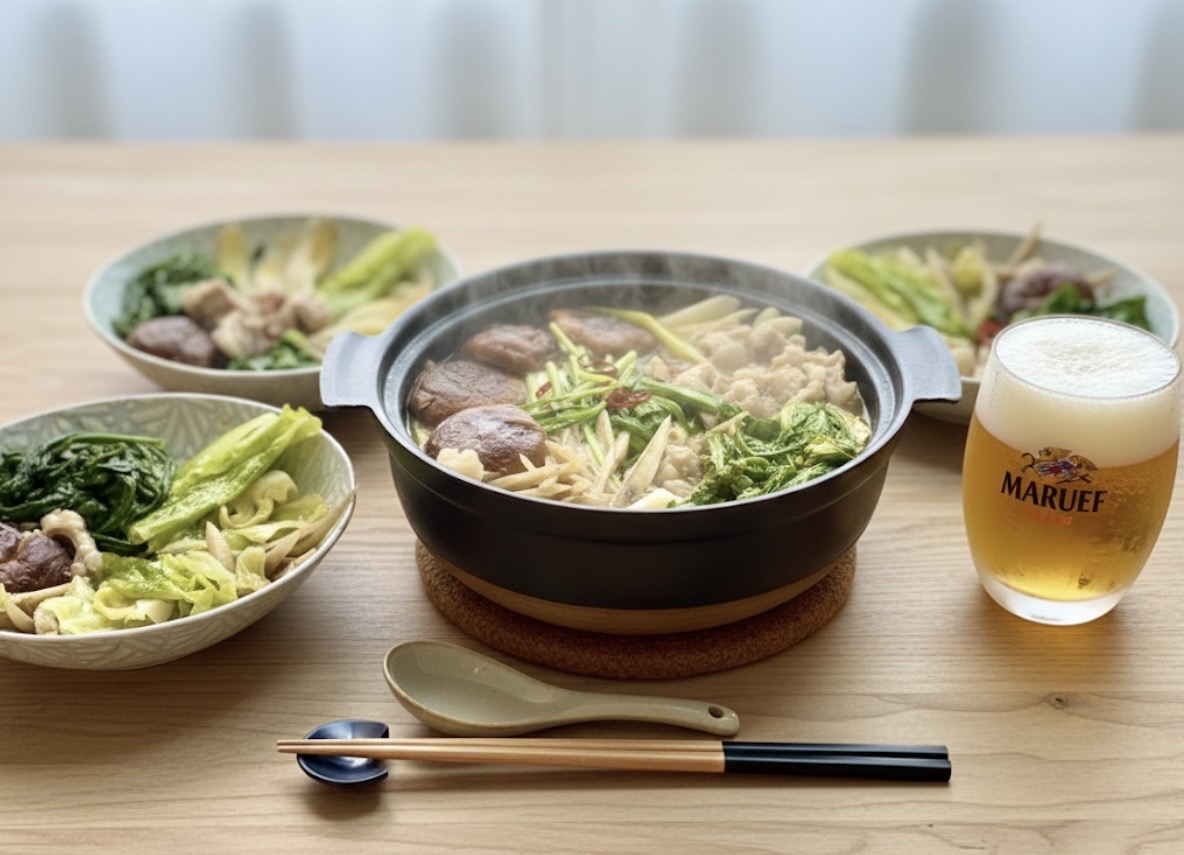 湯気が立ちのぼるもつ鍋を中心に、野菜と牛もつがたっぷり入った鍋料理と取り皿、横にマルエフの生ビールを並べた食卓風景