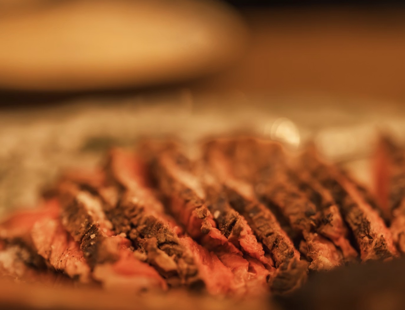 黒毛和牛ローストビーフの断面のクローズアップ写真。外側はスパイスが効いて香ばしく焼き色がつき、内側はしっとりとした美しいロゼ色に仕上がっている。背景は大きくぼかされており、重なり合ったお肉のジューシーな質感が際立っている。