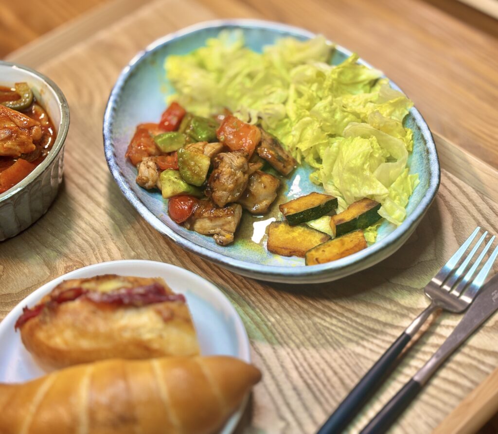 青い皿に、チキンとアボカドのオイスターソース炒め、焼きかぼちゃ、ちぎりレタスを盛り合わせ。赤いトマトと緑のアボカドが彩りよく見える。