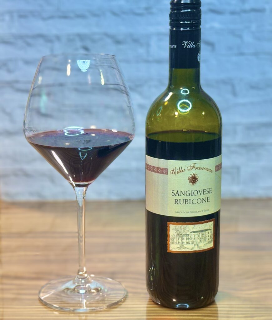 赤ワインの入ったワイングラスとボトルの並び。ラベルに「SANGIOVESE RUBICONE」と書かれたボトルがテーブルに立ち、落ち着いた家飲みの雰囲気。