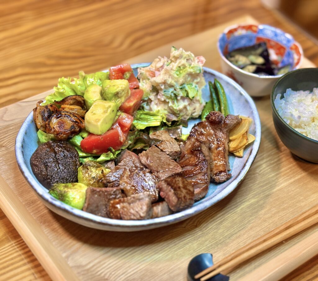 黒毛和牛のサイコロステーキと焼いた牛肉を中心に、ポテトサラダ、アボカドとトマトのサラダ、焼き野菜を盛り付けたメインプレートの写真。手前に艶のある牛肉、奥に副菜がバランスよく並び、食卓の温かい雰囲気が伝わる構図。