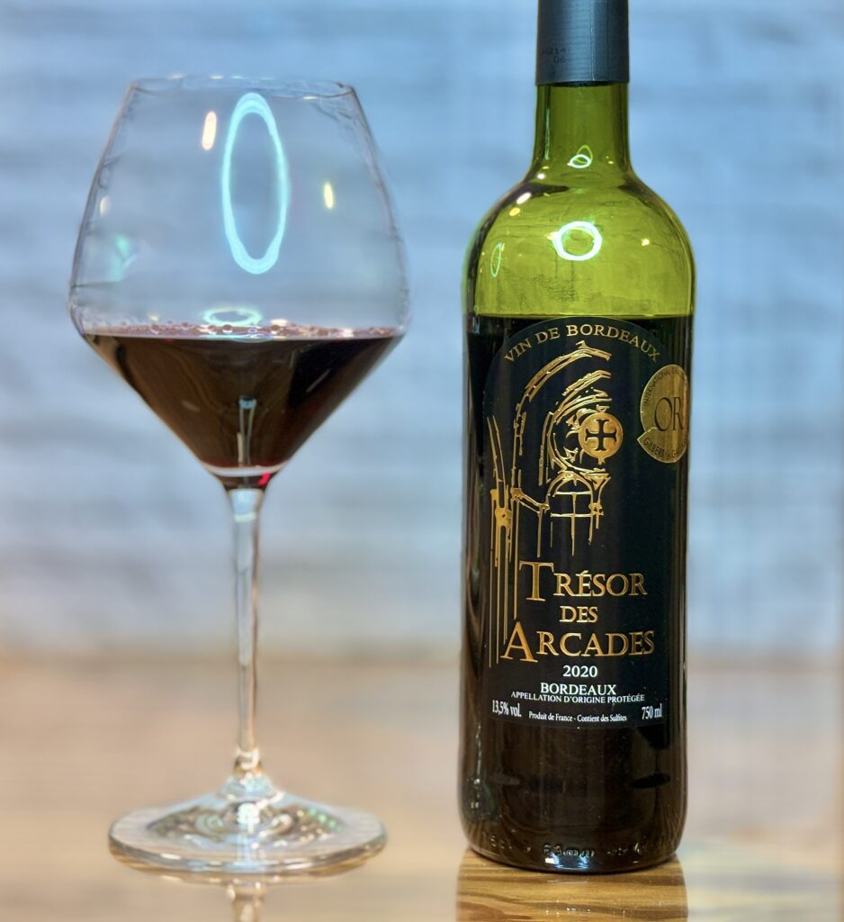 黒毛和牛のステーキに合わせた赤ワイン、ボルドー産「Trésor des Arcades 2020」のワインボトルと赤ワインを注いだワイングラスを並べた写真。ステーキディナーに合わせた食卓のワインペアリングを表現した一枚。