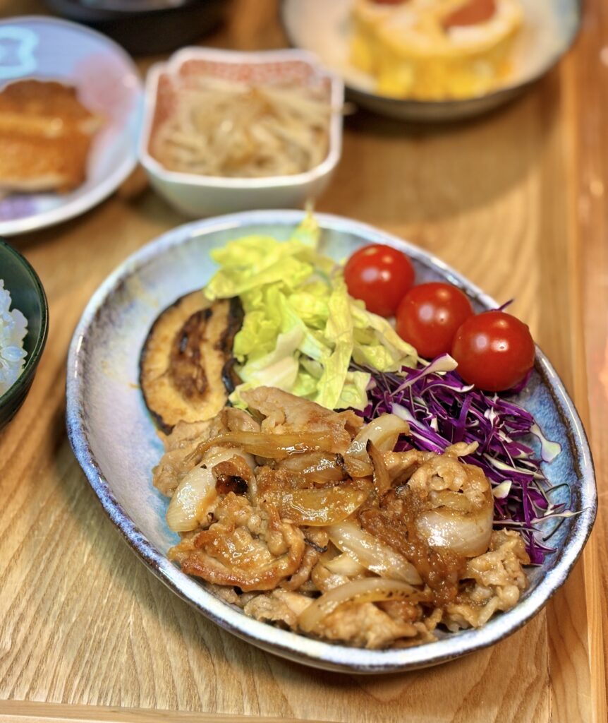 タモリ流豚の生姜焼きと玉ねぎ炒めを中心に、ミニトマト、レタス、紫キャベツ、焼きナスを添えた彩り豊かなメインプレートの料理写真。
