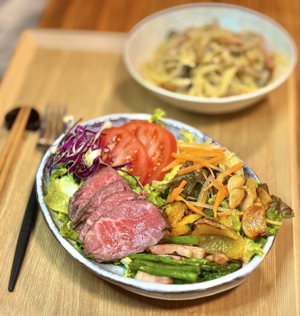 ローストビーフを主役にした彩りプレート。レアに仕上がったローストビーフのスライスに、トマト、紫キャベツ、レタス、焼きかぼちゃ、ベーコンとアスパラのガーリック炒め、人参の千切りが添えられた華やかなサラダプレート。