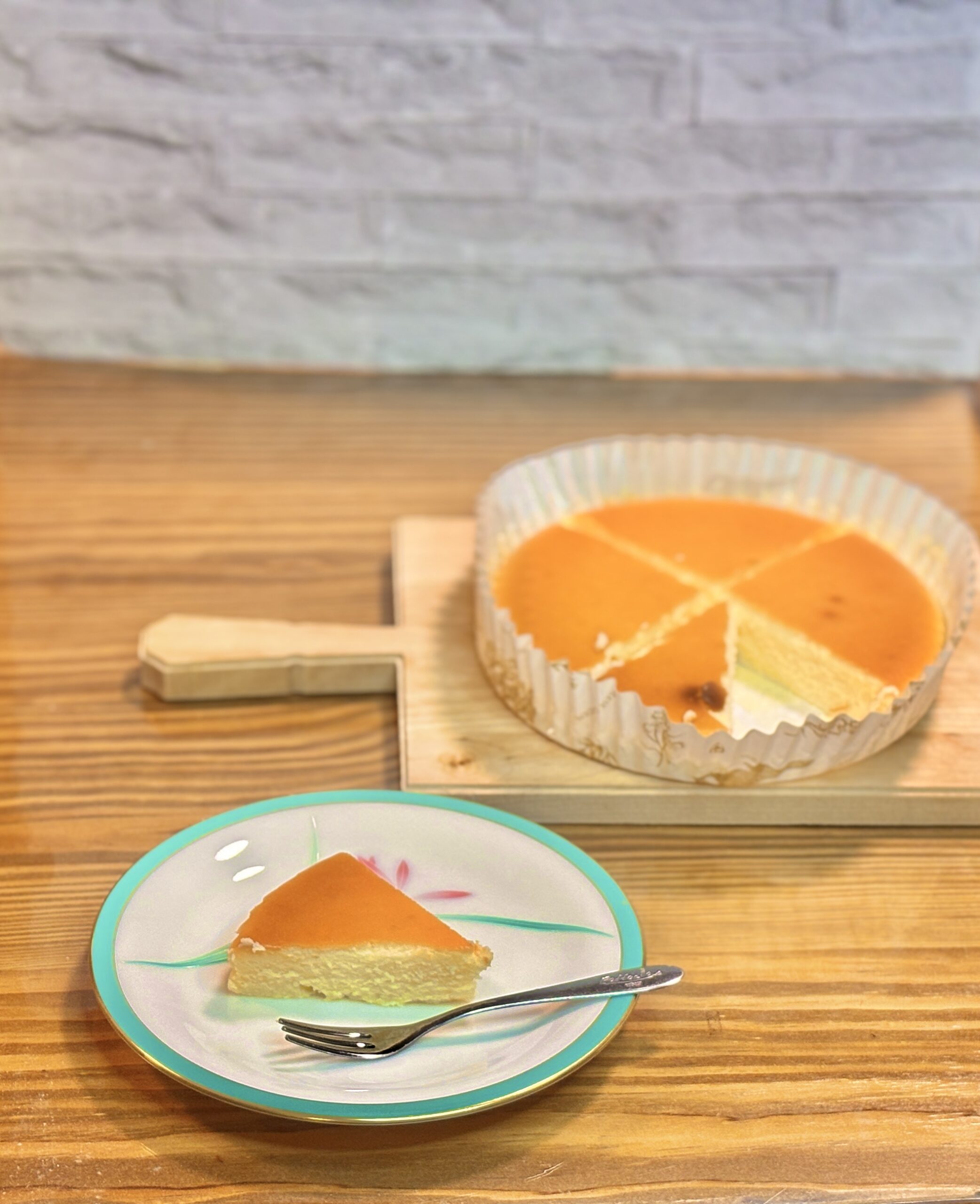 皿に盛り付けた御用邸チーズケーキのカットと、後ろにホールのチーズケーキ。しっとり濃厚な那須高原チーズガーデンの人気スイーツ。