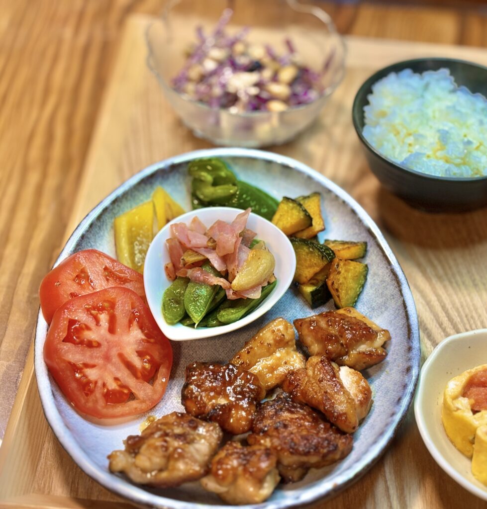 甘じょっぱいハニーマスタードチキンと彩り野菜のワンプレート料理。トマトスライス、焼きかぼちゃ、パプリカ、ピーマン、スナックえんどうとベーコンのガーリック炒めが盛られた家庭料理の夕食。