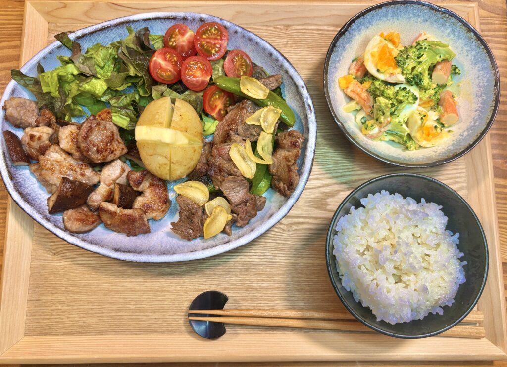 サイコロステーキとスナックえんどうのガーリック炒め、トンテキ椎茸焼き、じゃがバター、ミニトマトサラダに副菜のほぼカニとブロッコリーのマヨ和え、ご飯を並べた旦那キッチンの肉プレート定食。