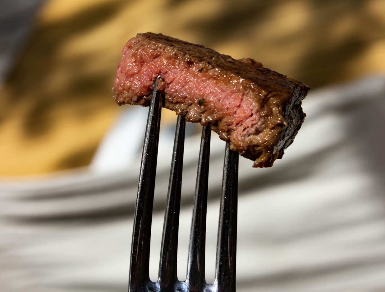 フォークで持ち上げたミディアムレアのサイコロステーキ。表面は香ばしく焼き色が付き、中はジューシーな赤身が見える牛肉のアップ写真。